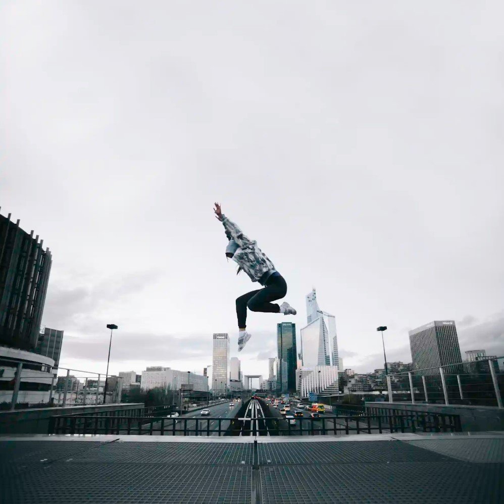 Young man jumping with hands up in the middle of a modern city, symbolizing enthusiasm, energy, and global reach